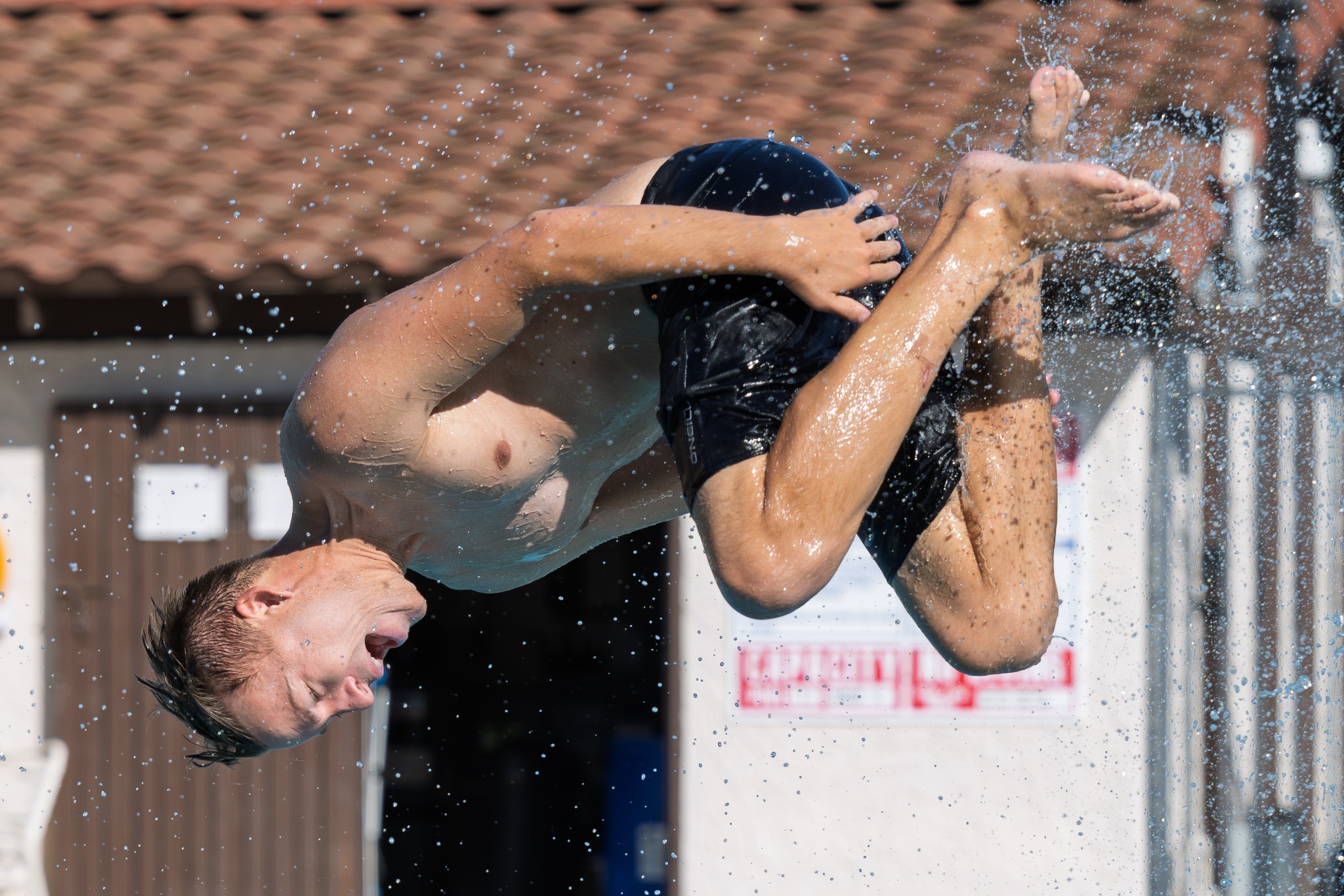 Swimmer performing a backflip above a swimming pool
