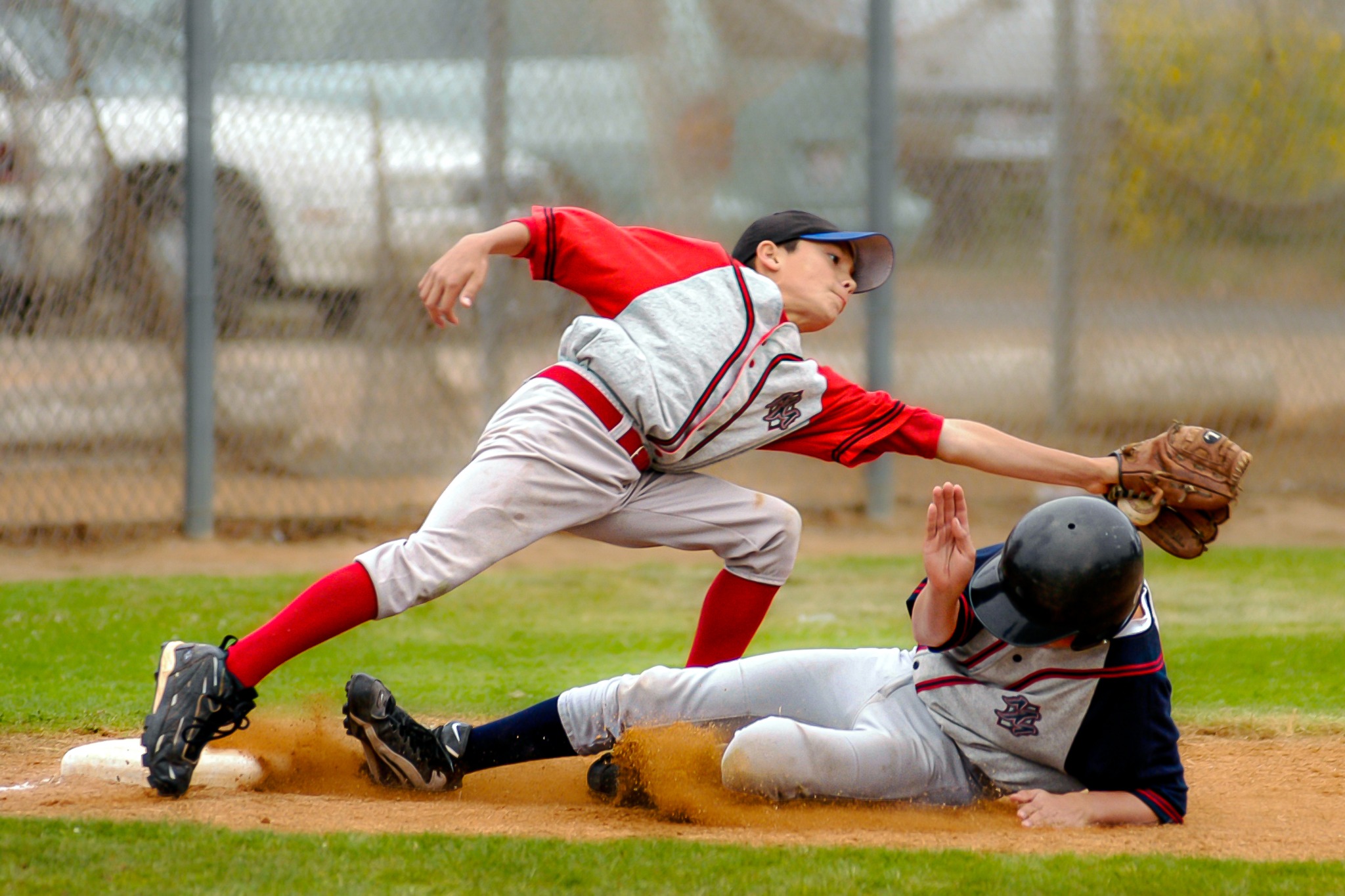 Baseball infielder stretching for a catch as a runner slides into second base